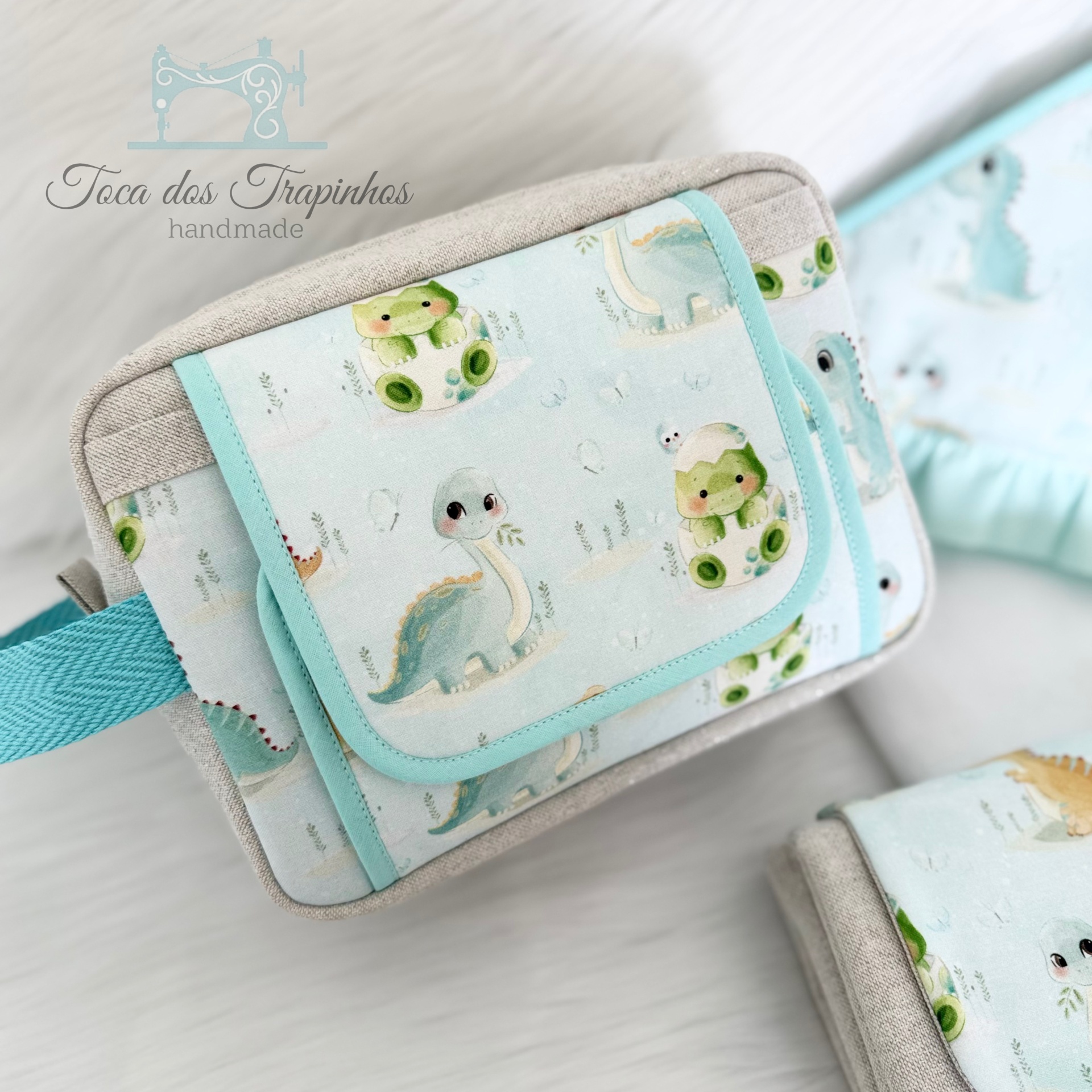 Bolsa infantil com padrão de dinossauros azuis e verdes em tecido