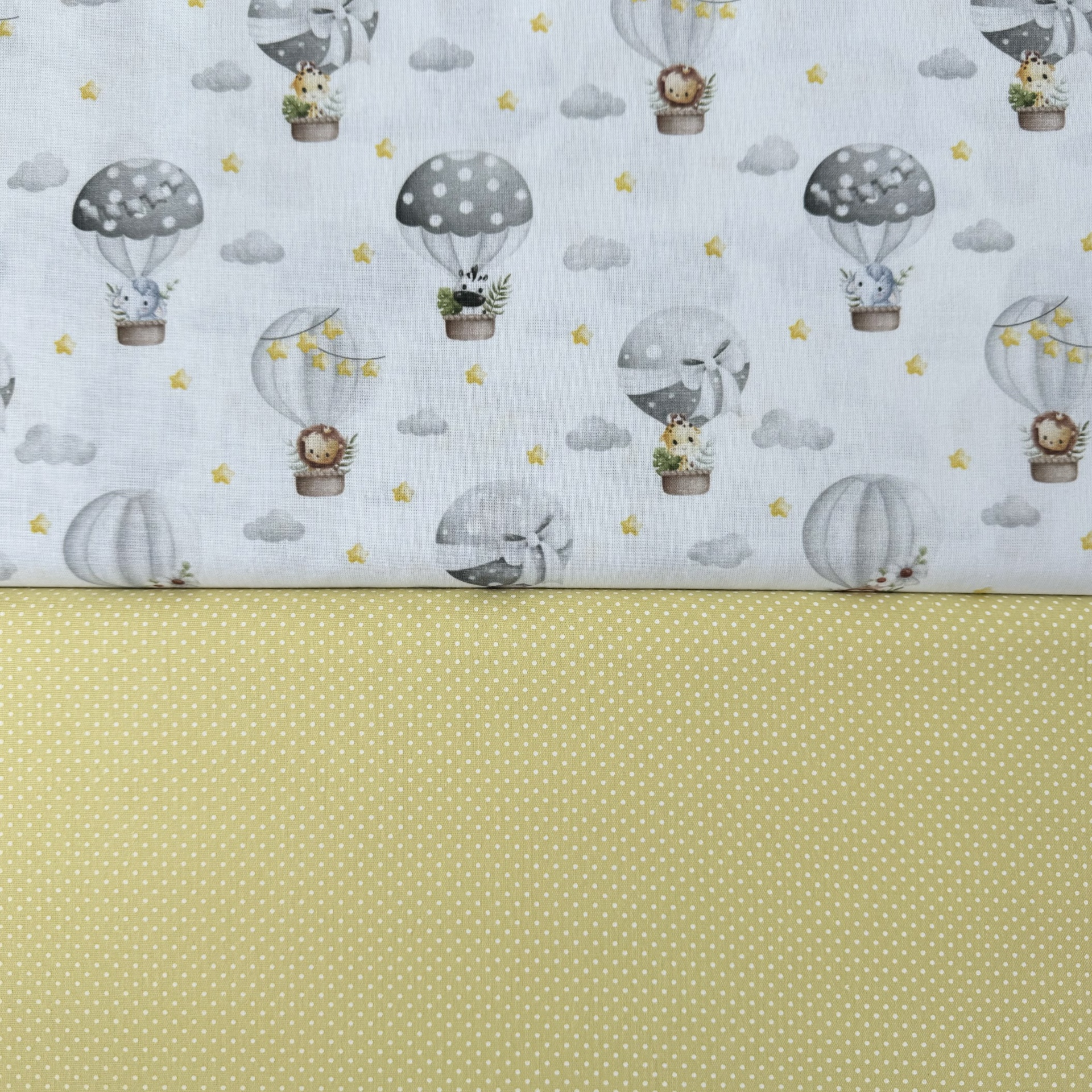 Tecidos com padrões de balões com animais e bolinhas brancas sobre fundo amarelo claro.