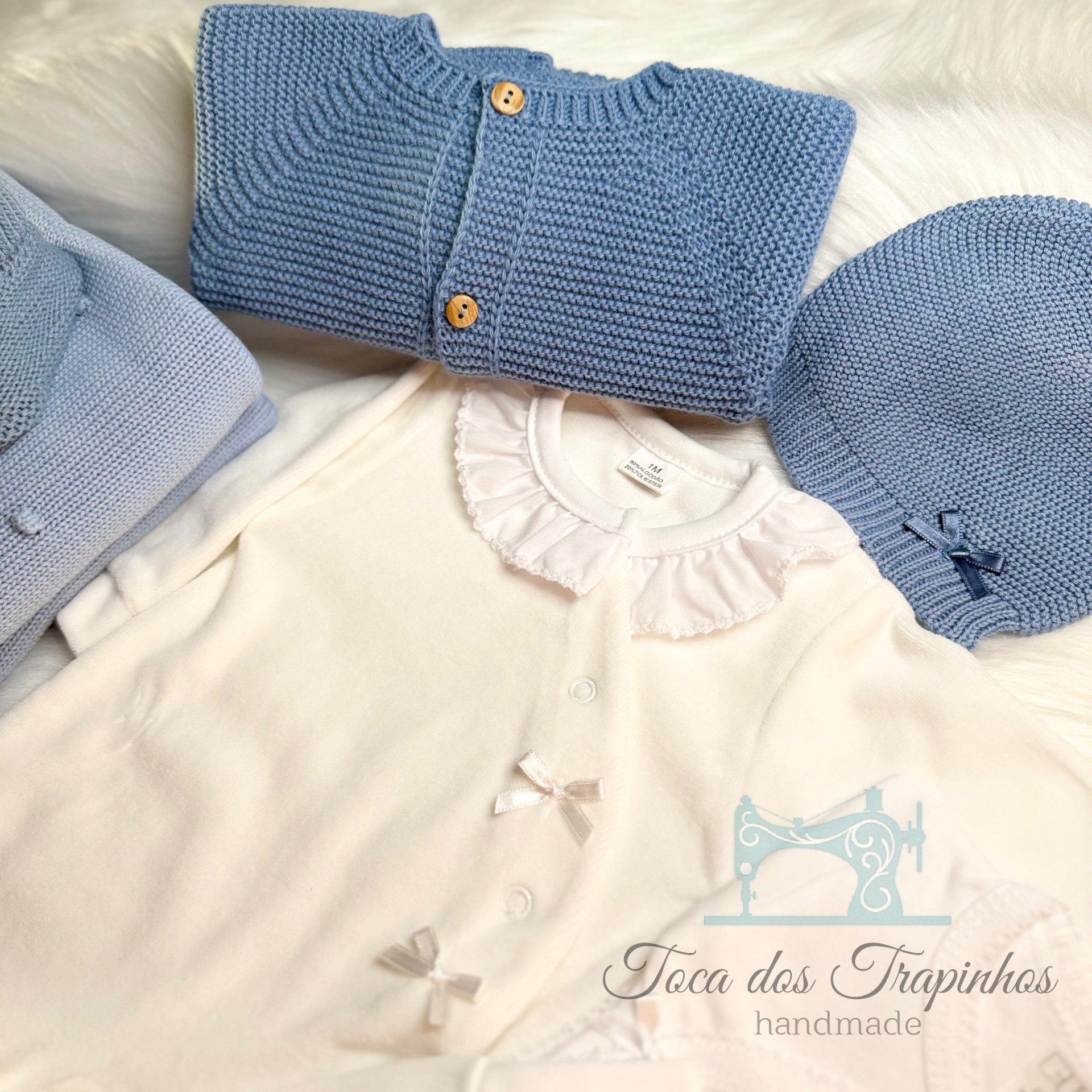 Conjunto de roupa para bebé azul e branco com casaco, touca e body sobre fundo branco felpudo