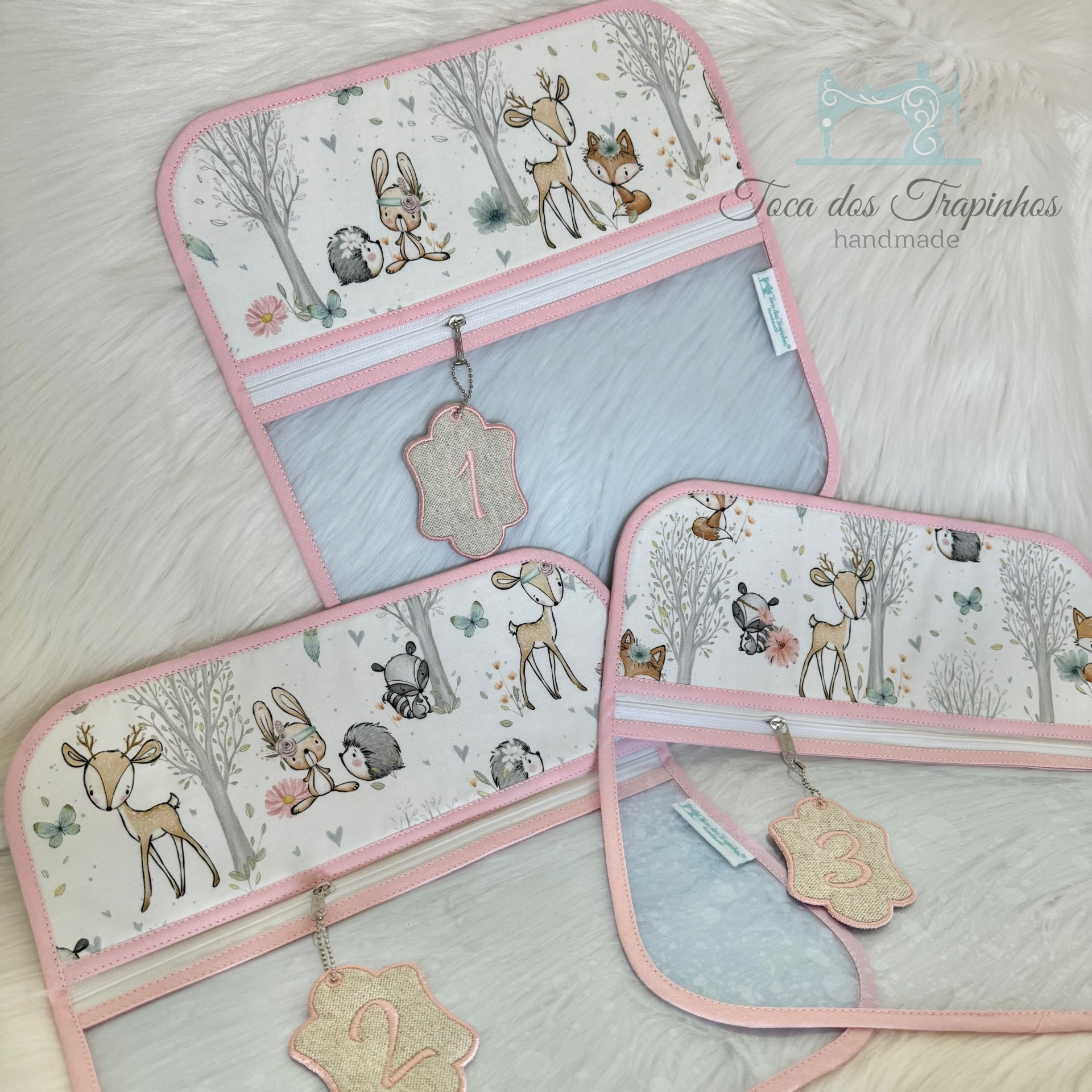 Três organizadores de tecido com padrão de animais da floresta e bordas rosa e azul claro