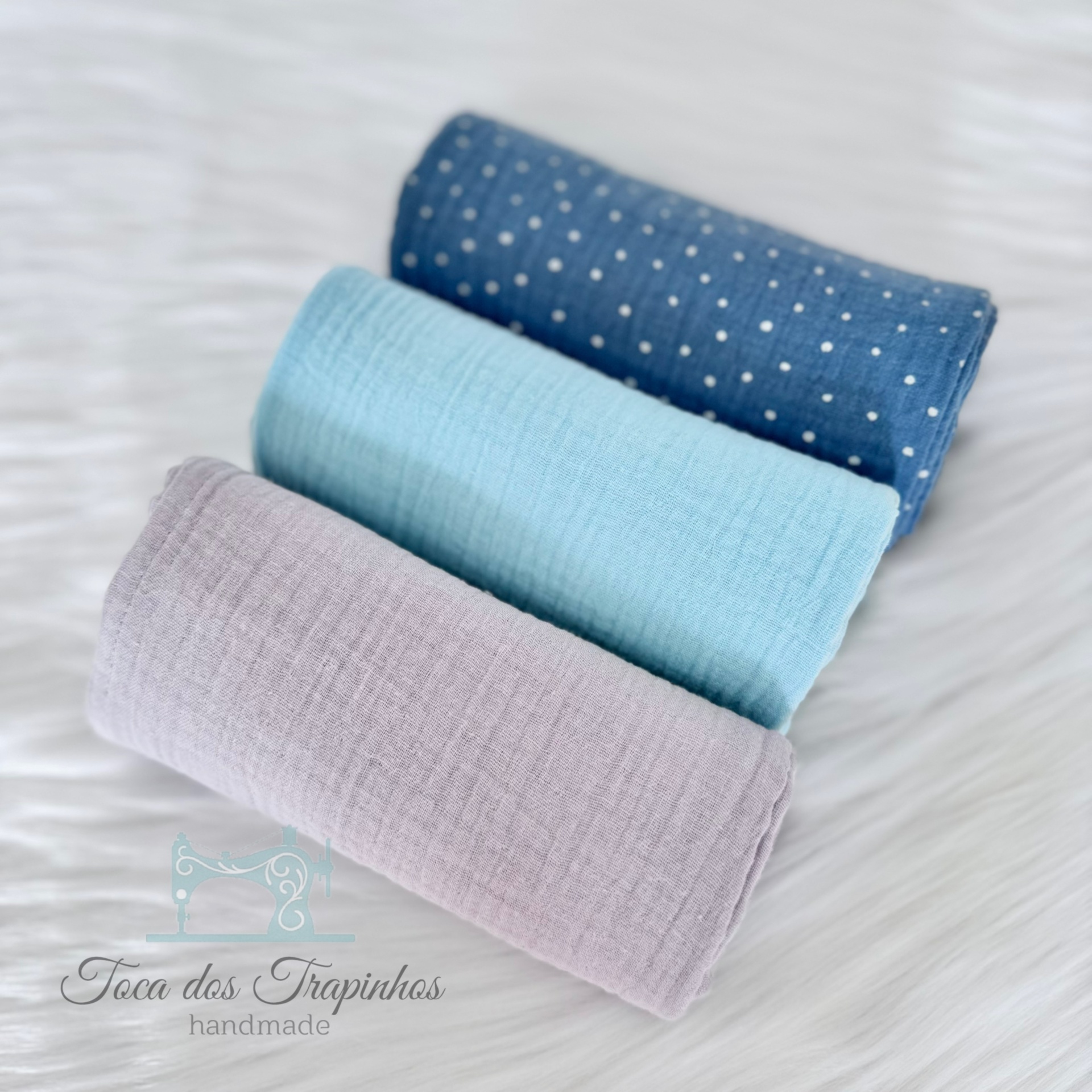 Três panos de tecido em azul escuro com bolinhas, azul claro e lilás sobre superfície branca