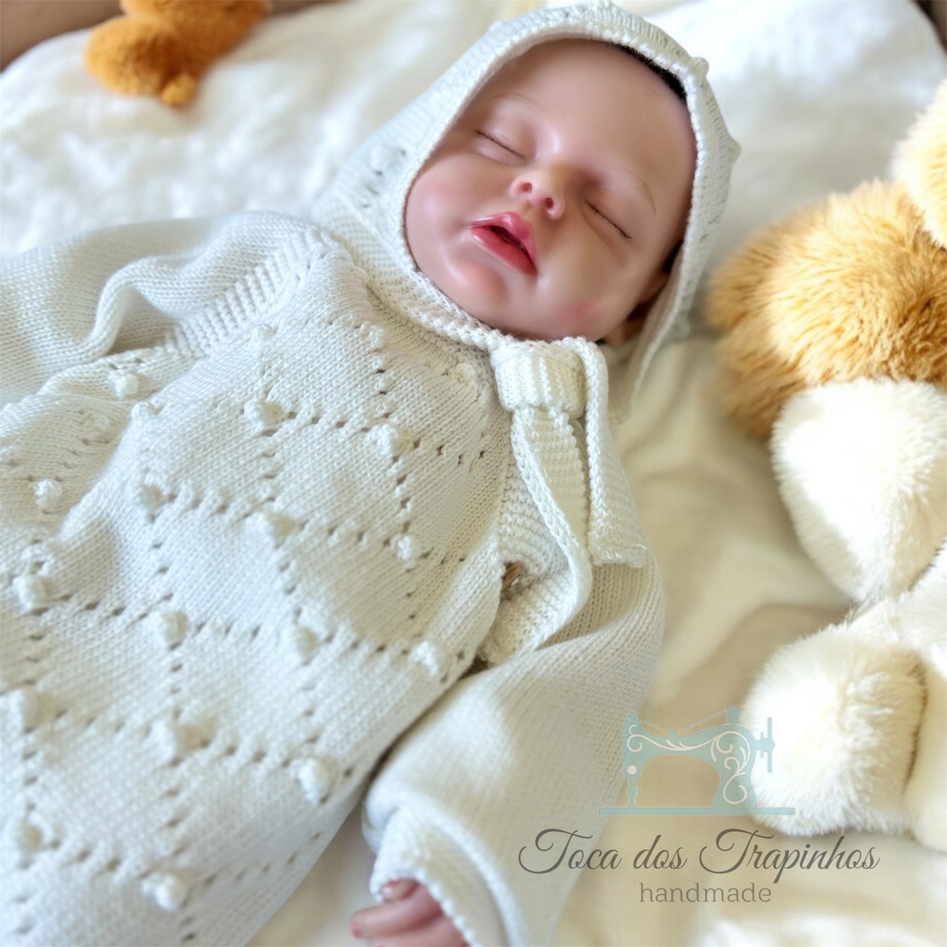 bebé em macacão branco de malha com capuz e peluches