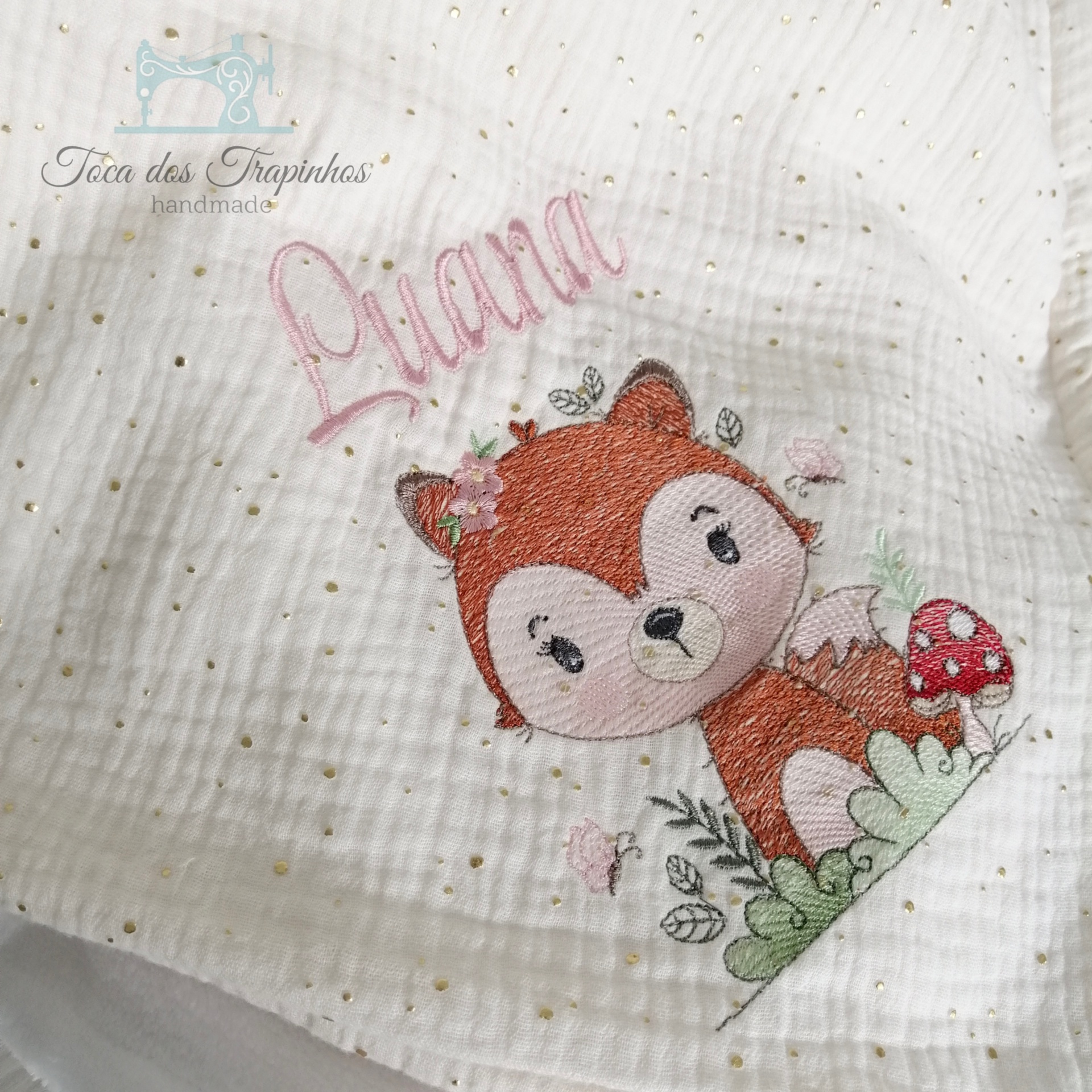 Pano branco com bordado de raposa, cogumelo e o nome Luana em rosa.