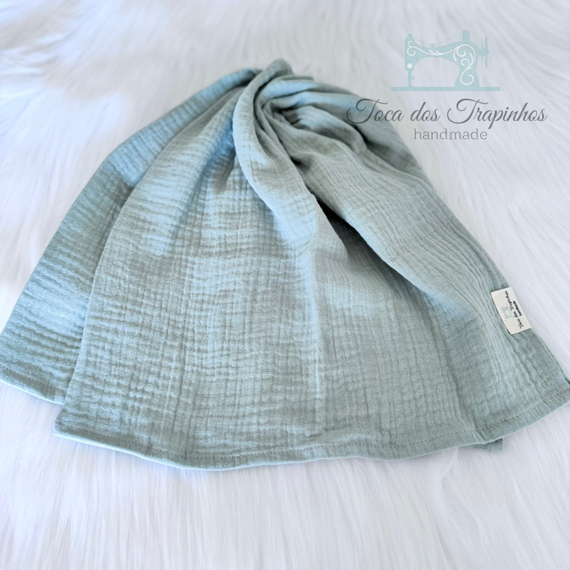 Manta cinza claro de muselina com etiqueta branca sobre fundo branco felpudo