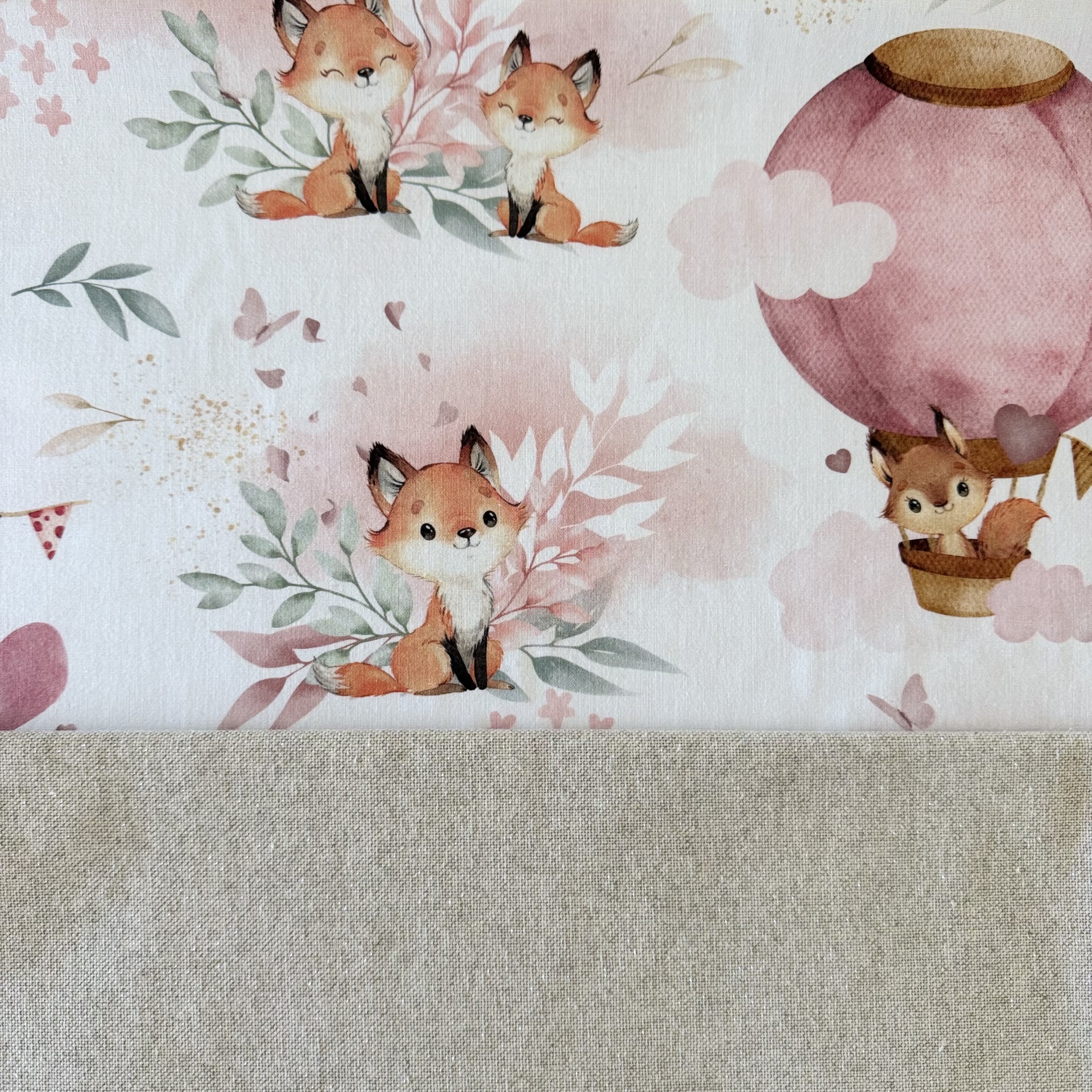 Tecido branco com padrão de raposas e balão de ar quente rosa sobre fundo bege
