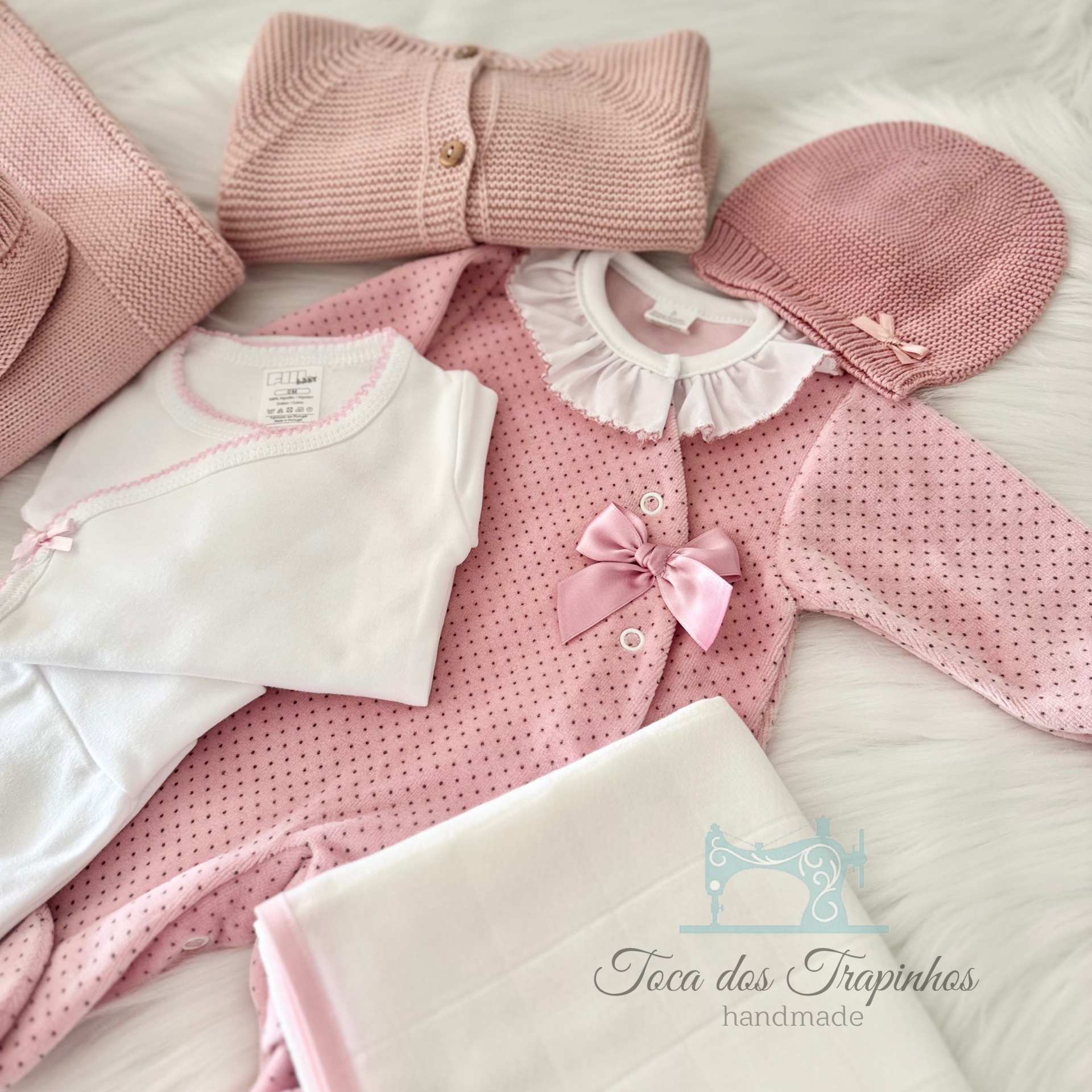 Conjunto de roupa de bebé rosa e branca artesanal com vários itens em malha e tecido sobre fundo branco