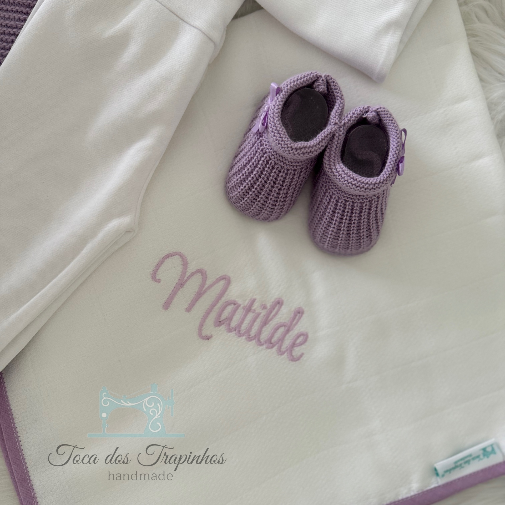 Manta branca bordada com o nome Matilde e sapatinhos de croché lilás