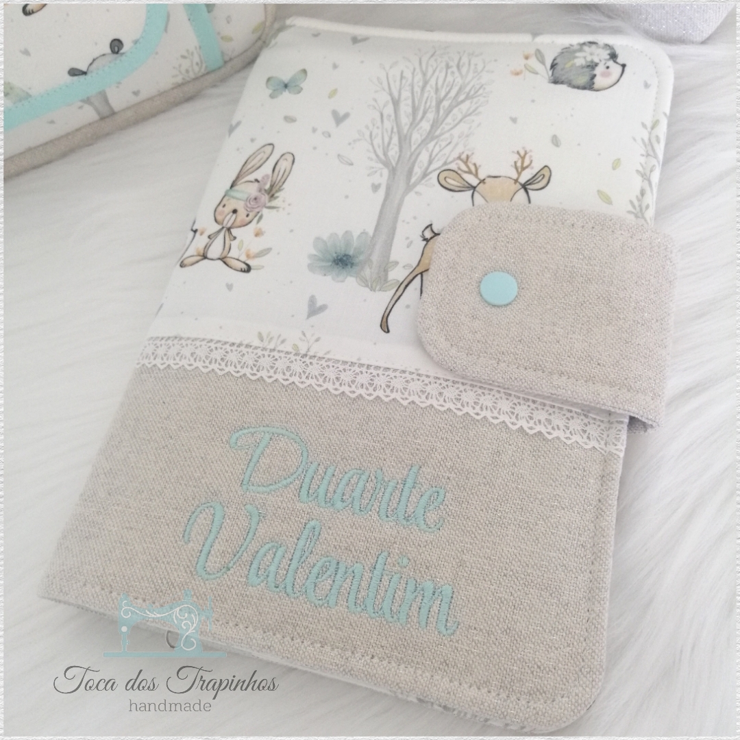 Capa decorativa em tecido bege e branco com ilustrações de animais e texto bordado