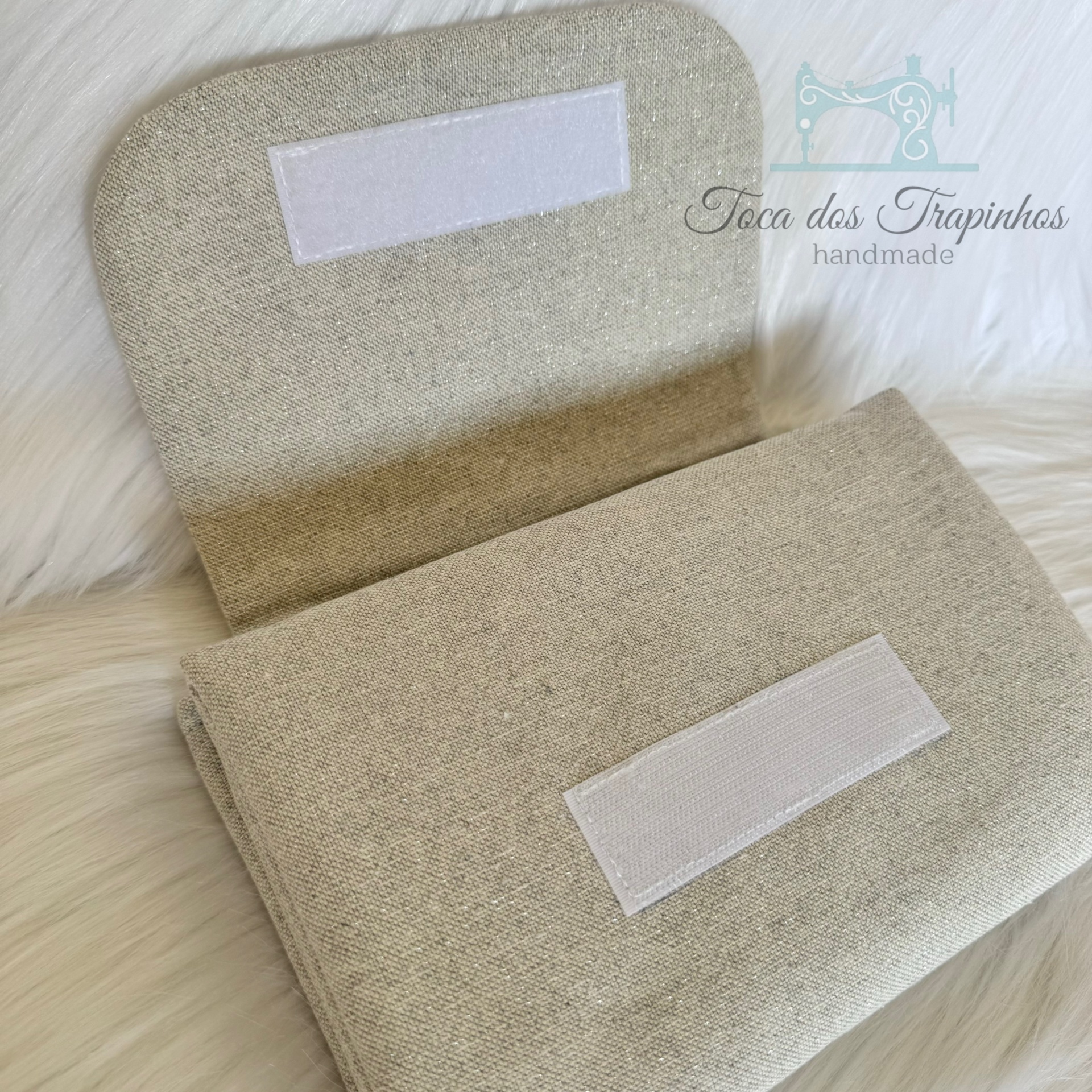 Carteira de tecido bege claro com fecho de velcro e logo com texto Toca dos Trapinhos handmade