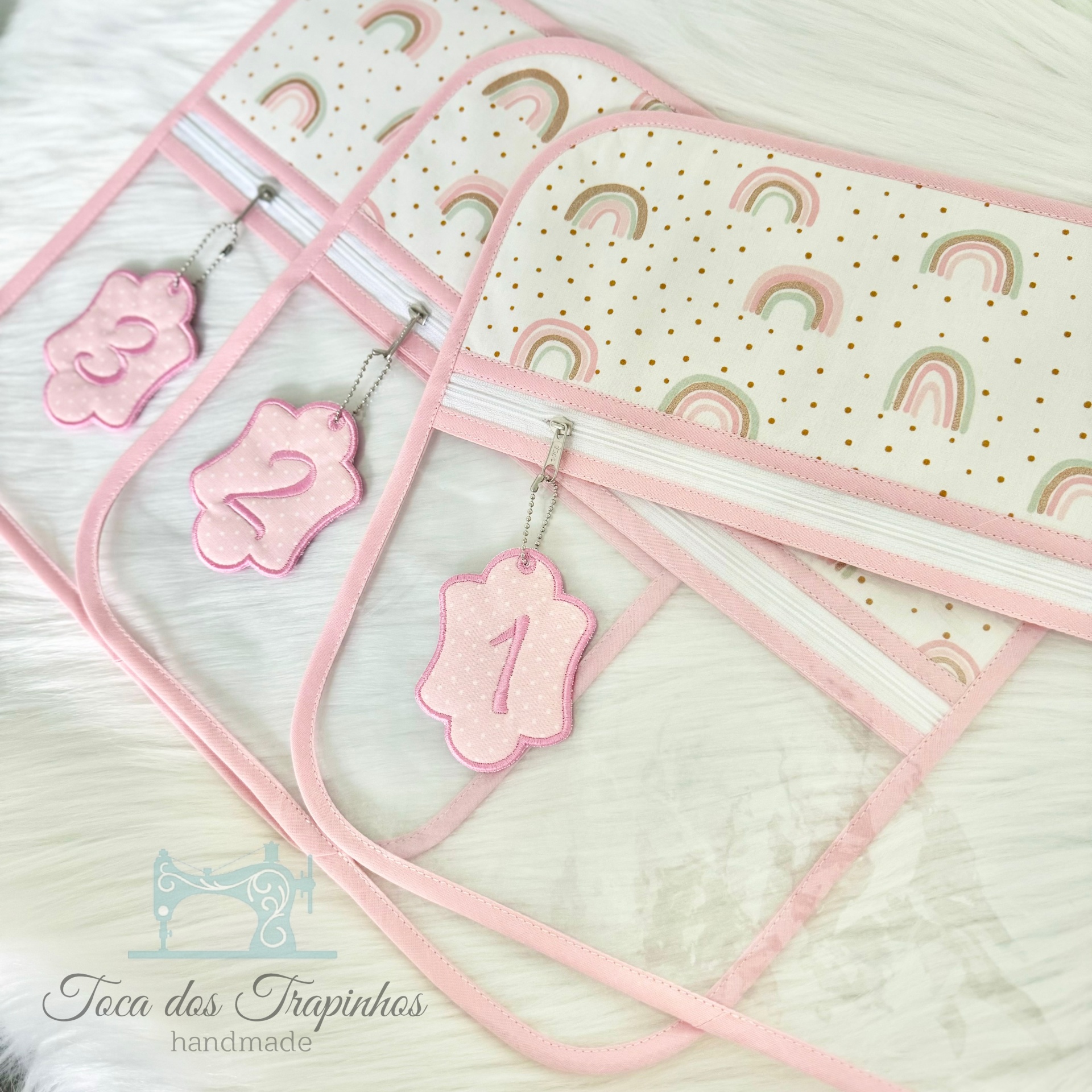 Três bolsas transparentes com acabamento rosa e padrão de arcos-íris e pontos dourados