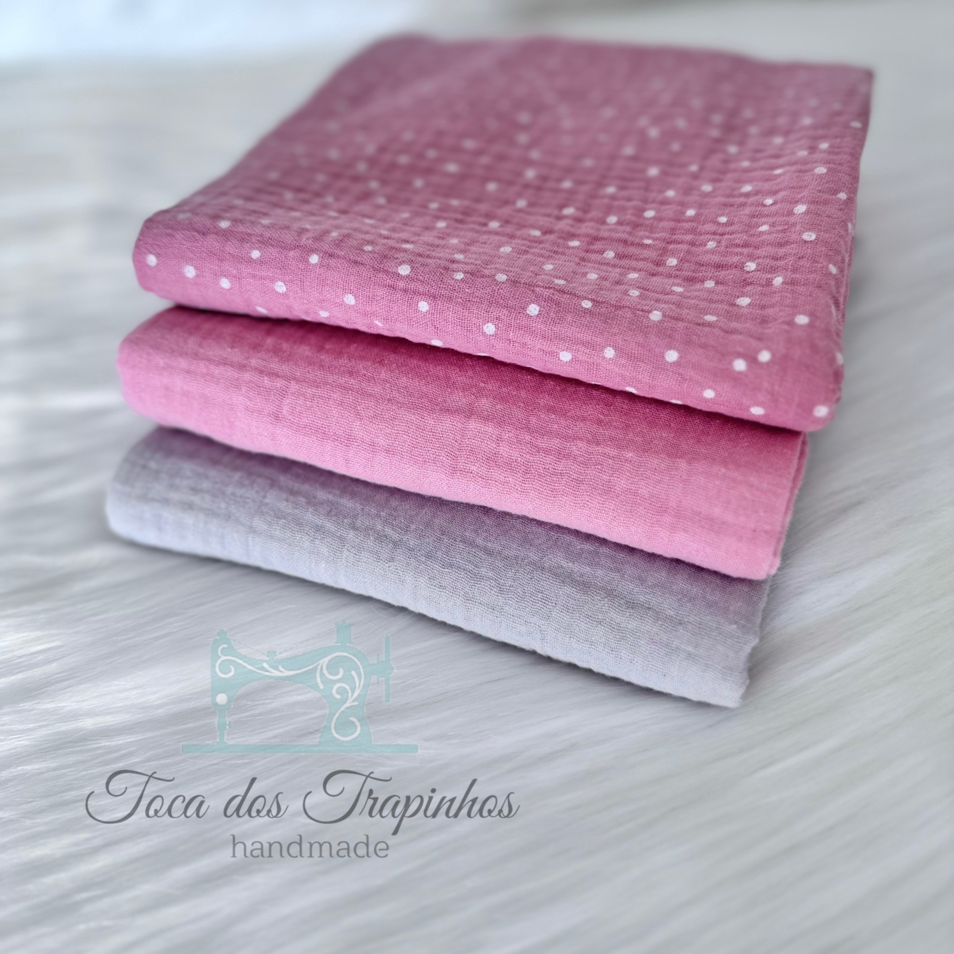 Três tecidos dobrados em rosa com bolinhas, rosa liso e cinza claro sobre fundo branco