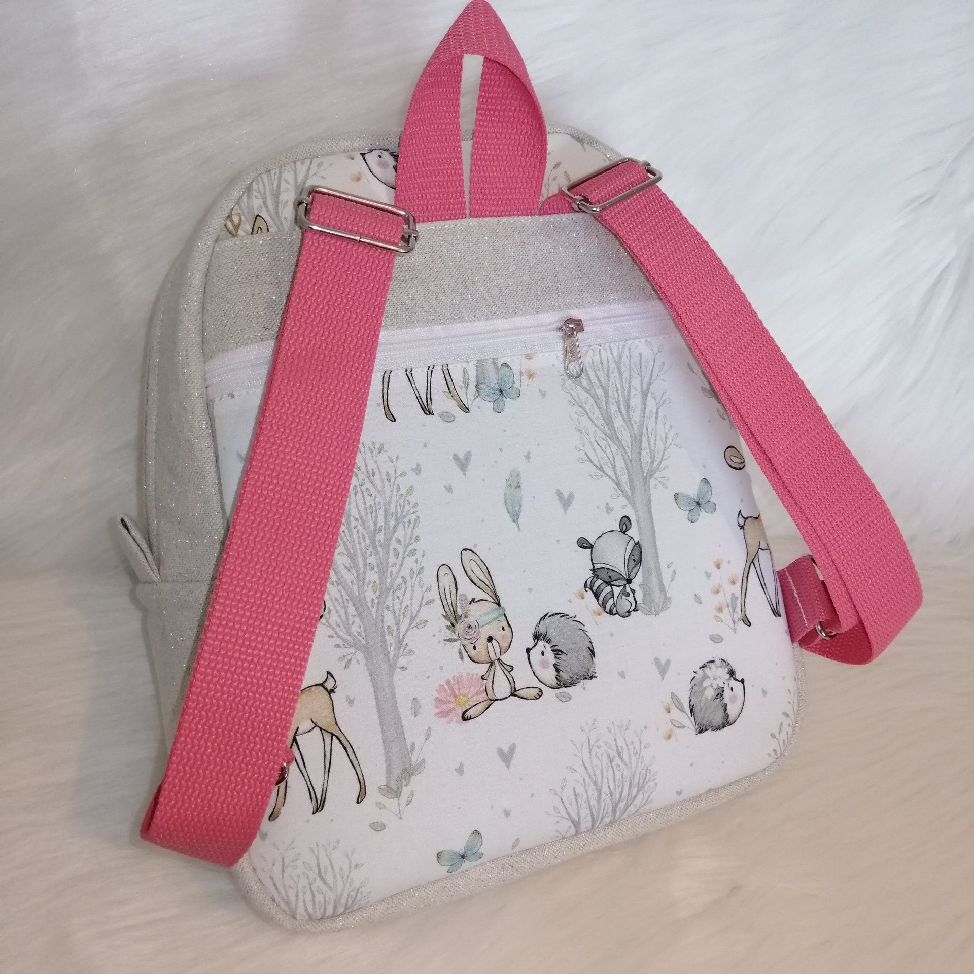 Mochila infantil pequena com alças rosas e padrão de animais e árvores em tons suaves