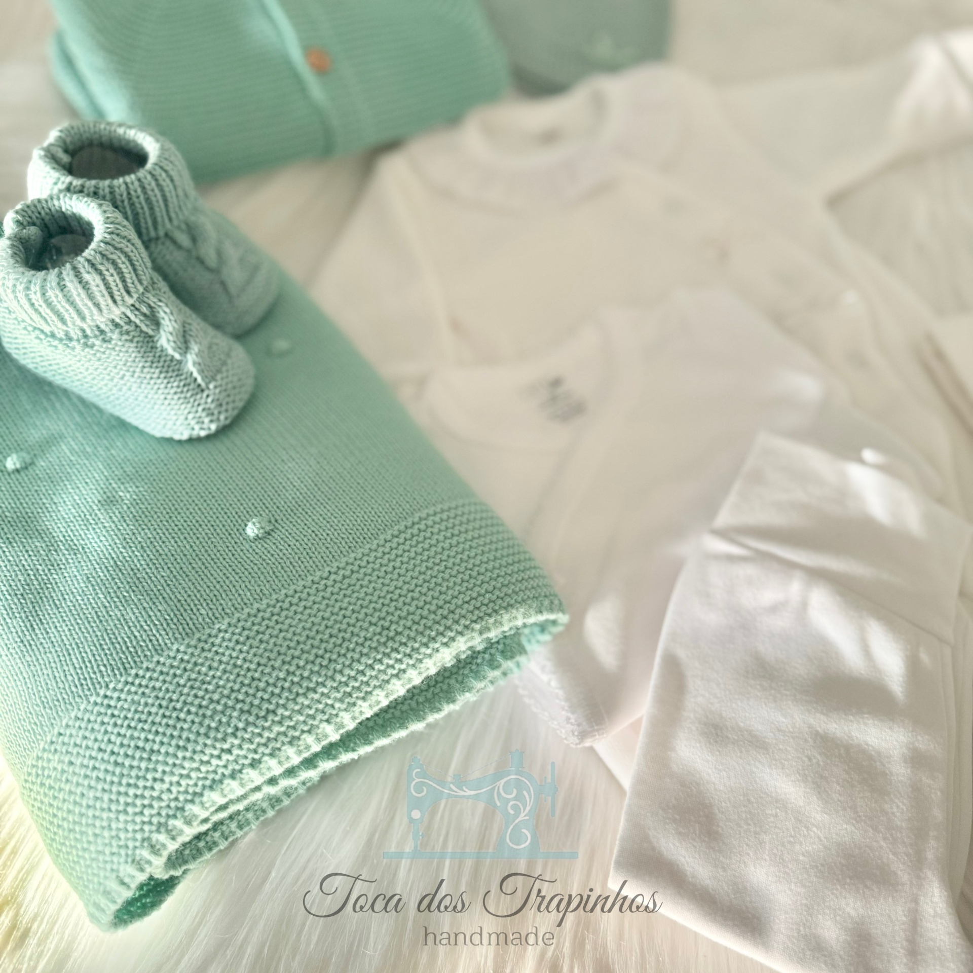 Conjunto de roupa de bebé com manta verde água, meias verdes e roupas brancas sobre superfície branca