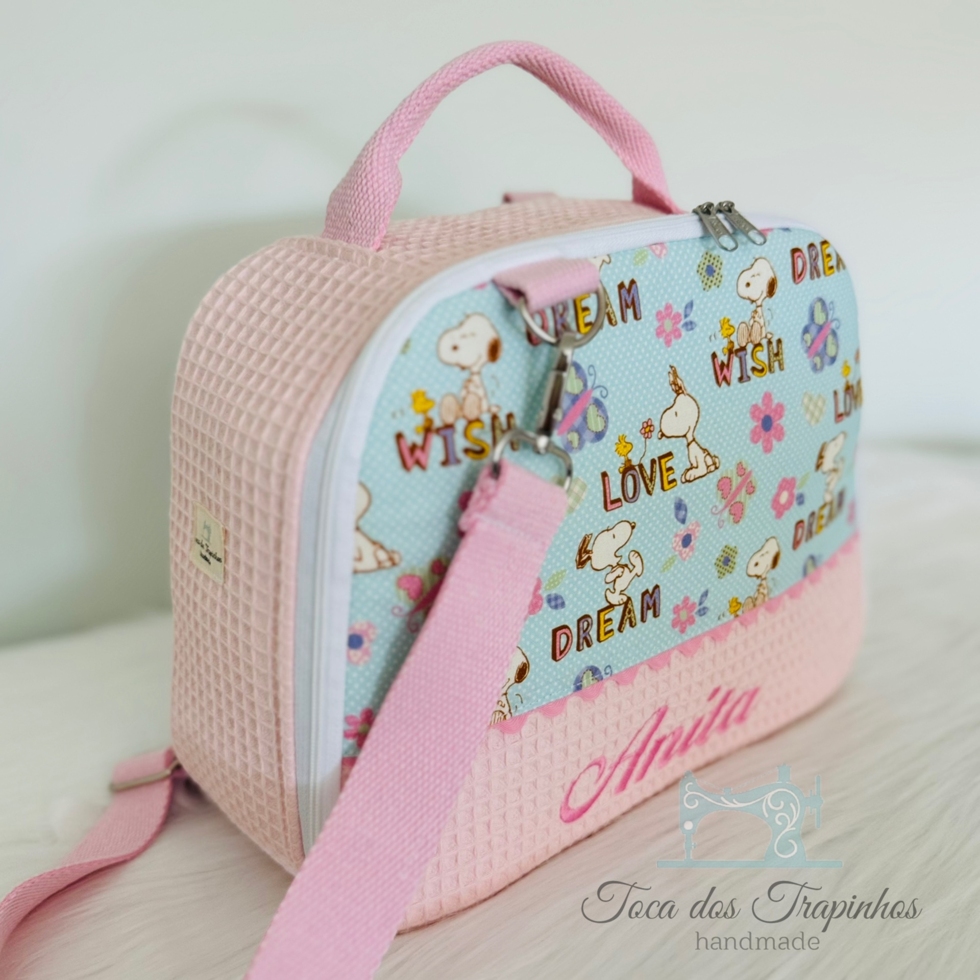 Mala infantil rosa e azul com padrão Snoopy e nome Anita bordado.