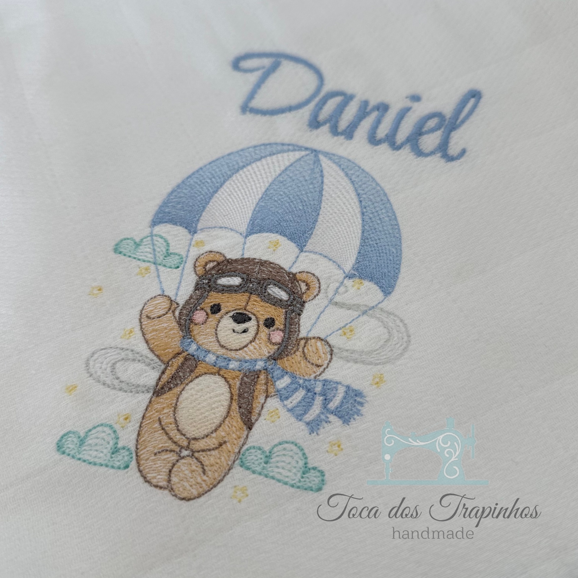 Toalha branca bordada com ursinho aviador e paraquedas azul, texto 'Daniel'