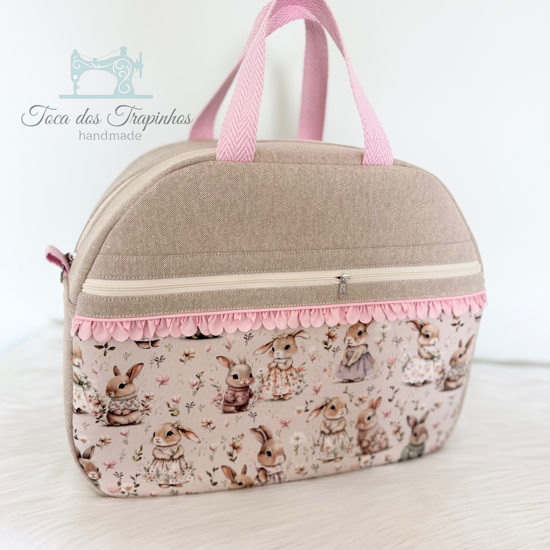 Mala bege com padrão de coelhinhos vestidos e franja rosa.