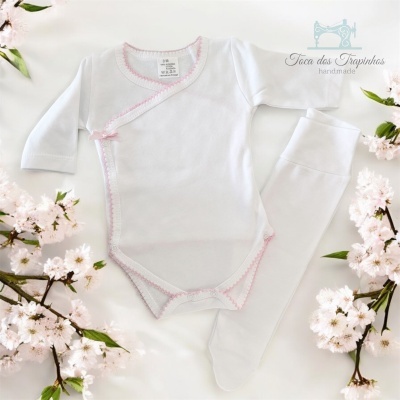 Conjunto de bebé branco com detalhes rosa rodeado de flores brancas e rosas