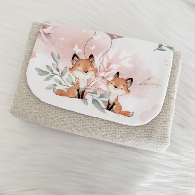 Carteira em tecido bege com aba branca decorada por ilustração de duas raposas e elementos florais