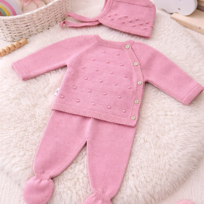 Conjunto de bebé rosa em malha com camisola, calças e gorro sobre tapete branco