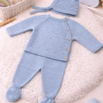 Roupa de bebé azul clara em malha com camisola, calças e gorro sobre tapete felpudo branco