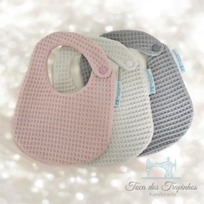 Três babetes de tecido texturizado nas cores rosa, bege e cinza