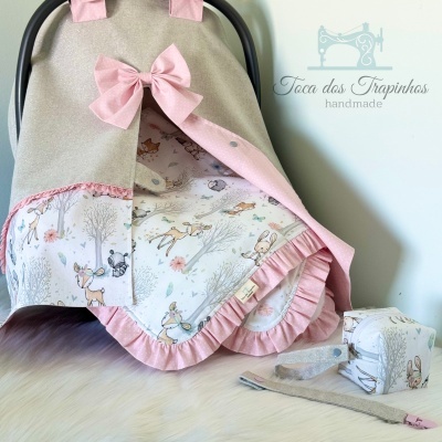 Capa para cadeirinha de bebé bege e rosa com tecidos estampados e acessórios na superfície clara