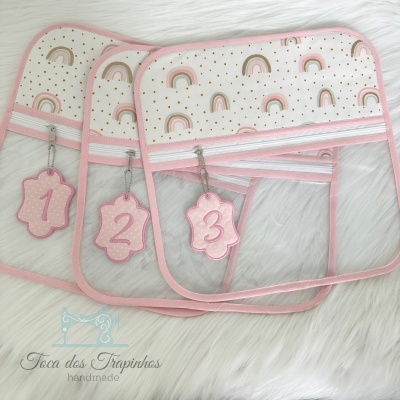 Três organizadores transparentes com bordas e estampas rosa e chaveiros numerados em fundo branco peludo