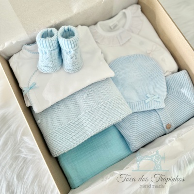 Conjunto de roupa de bebé azul claro e branco numa caixa com etiqueta
