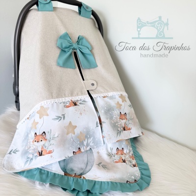 Capa para carrinho de bebé bege com laço azul esverdeado e padrão de raposas e estrelas.