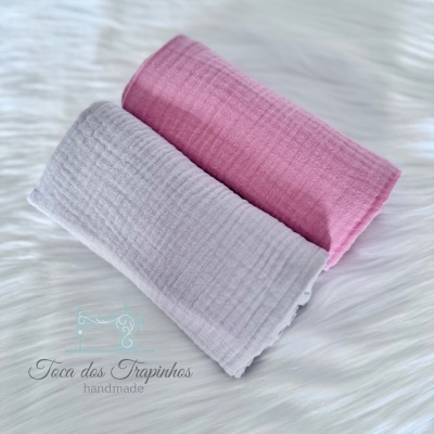 Dois panos de algodão rosa e cinza com textura canelada sobre superfície branca macia com logo 'Toca dos Trapinhos handmade'.