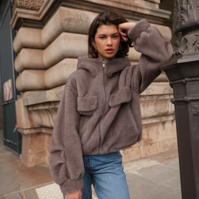 Mulher com casaco de pelo castanho claro e jeans azuis segurando mala vermelha em rua urbana