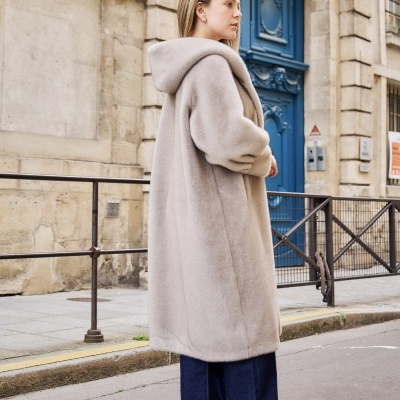 Casaco comprido cinza claro de tecido peludo com capuz usado numa rua diante de um edifício.