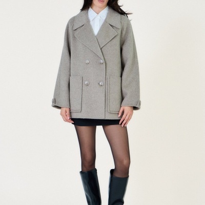 Mulher a usar casaco cinzento claro com botões duplos e botas pretas até à canela