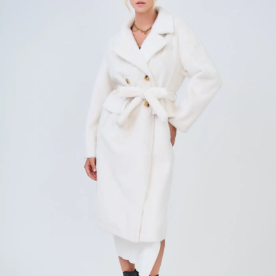 Mulher a usar casaco comprido branco felpudo com cinto, botas pretas e vestido branco.