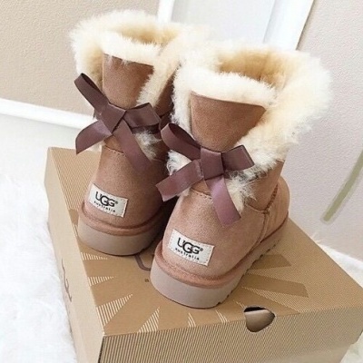 Botas UGG caramelo com pelo branco e laço castanho sobre caixa de cartão