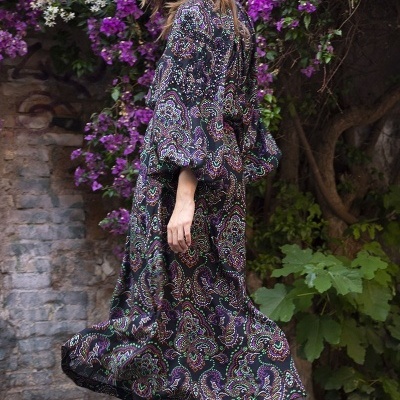 Mulher de vestido comprido com padrão floral colorido e botas pretas em jardim florescente.