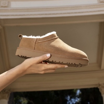 Botas castanhas com interior branco de pêlo sendo seguradas por uma mão