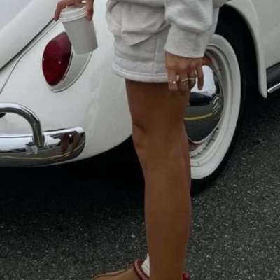 Pessoa com roupa cinzenta e sapatilhas castanhas ao lado de carro clássico branco