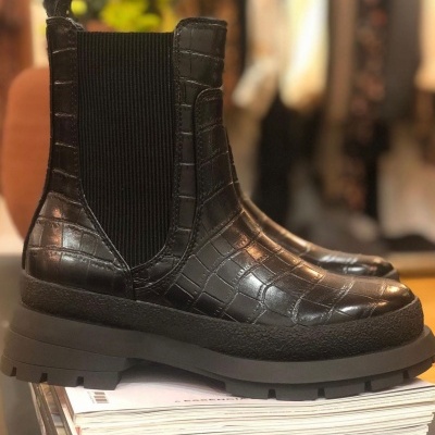Botas negras estilo Chelsea com textura de pele croco sobre revistas