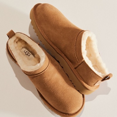 Chinelos castanhos em camurça com interior de pelo branco e sola castanha, marca UGG.