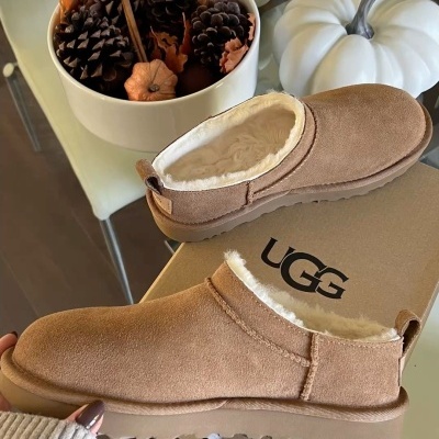 Pantufas UGG castanhas com forro branco sobre caixa UGG e decoração com pinhas, abóboras e vela acesa