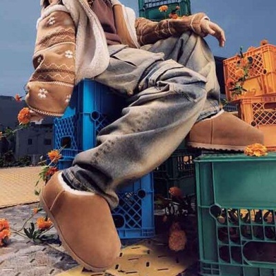 Pessoa com botas castanhas de camurça sentada em caixas plásticas coloridas rodeada de flores laranja