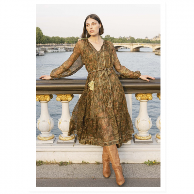 Vestido floral castanho e verde com mangas compridas, usado com botas castanhas perto de rio e ponte.