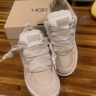 Sapatilhas UGG bege com pelo branco e atacadores largos xadrez sobre mesa de madeira