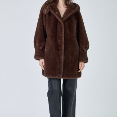 Mulher vestindo casaco de pelo sintético castanho, calças pretas e sapatos com laço