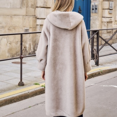 Casaco comprido bege de pelo sintético com capuz, visto de costas, num ambiente urbano.