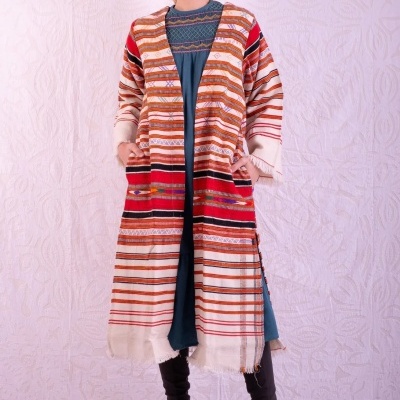 Casaco comprido de malha riscada em tons quentes, usado com vestido azul e botas pretas.