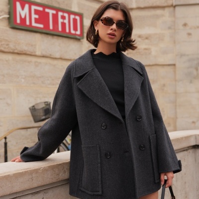 Mulher com casaco cinzento escuro de lã e óculos de sol junto a sinal METRO