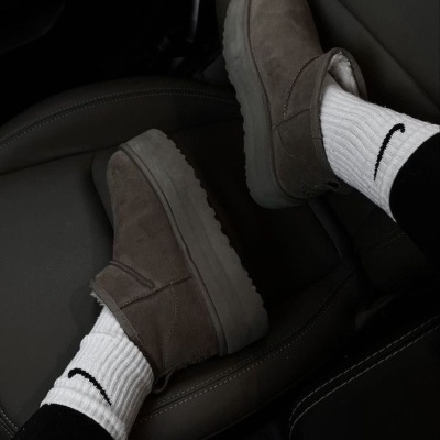 Botas cinza de camurça com sola branca e meias Nike brancas num banco de carro de couro