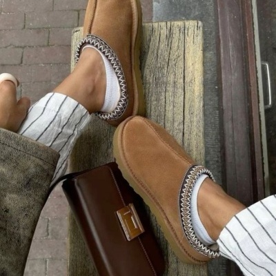 Chinelos castanhos com padrão zigzag ao lado de mala de mão castanha sobre banco de madeira.